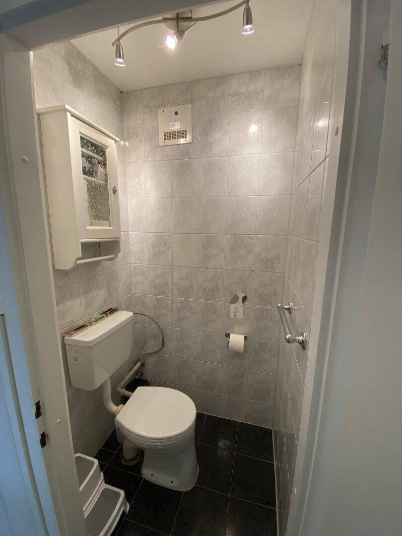 Kleines Gäste-WC mit Fliesen an Wänden und Boden sowie einem Lüfter.