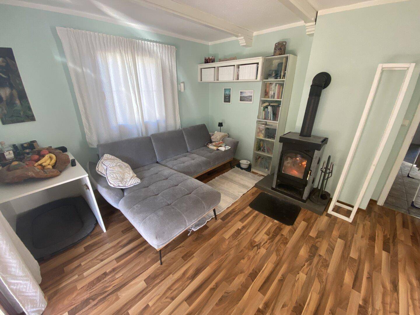 Gemütliches Wohnzimmer mit Holzboden, Ecksofa und einem wärmenden Holzofen.
