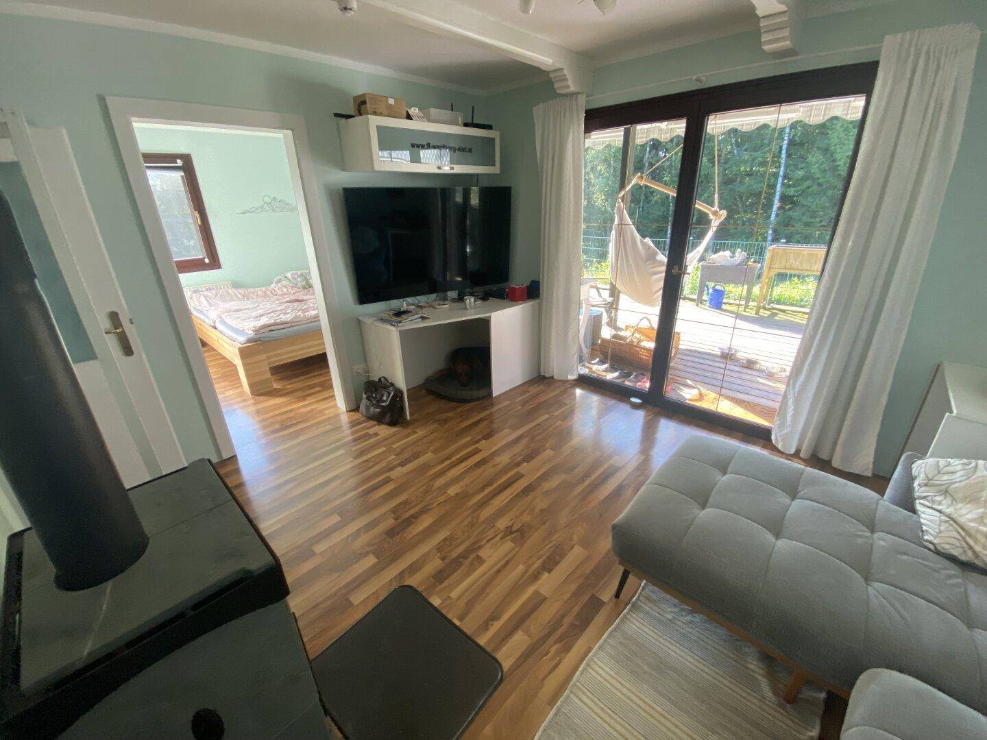 Helles Wohnzimmer mit Holzboden, Terrassenzugang und Blick in ein angrenzendes Schlafzimmer.