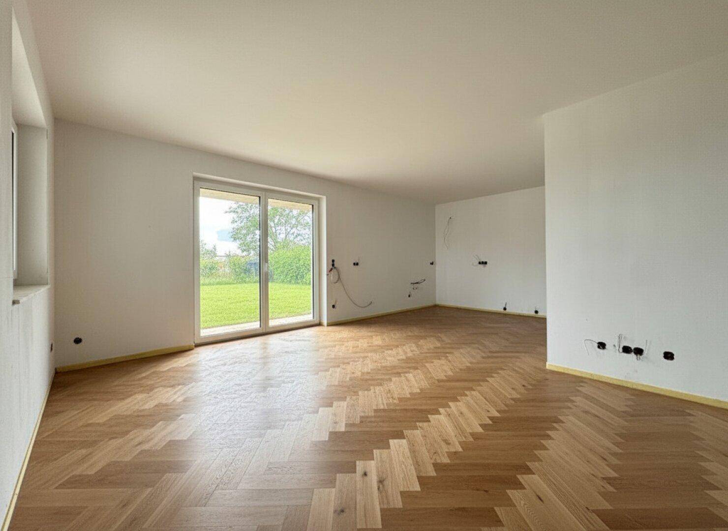 Heller, leerer Raum mit Fischgrätparkett und großem Fenster zum Garten.