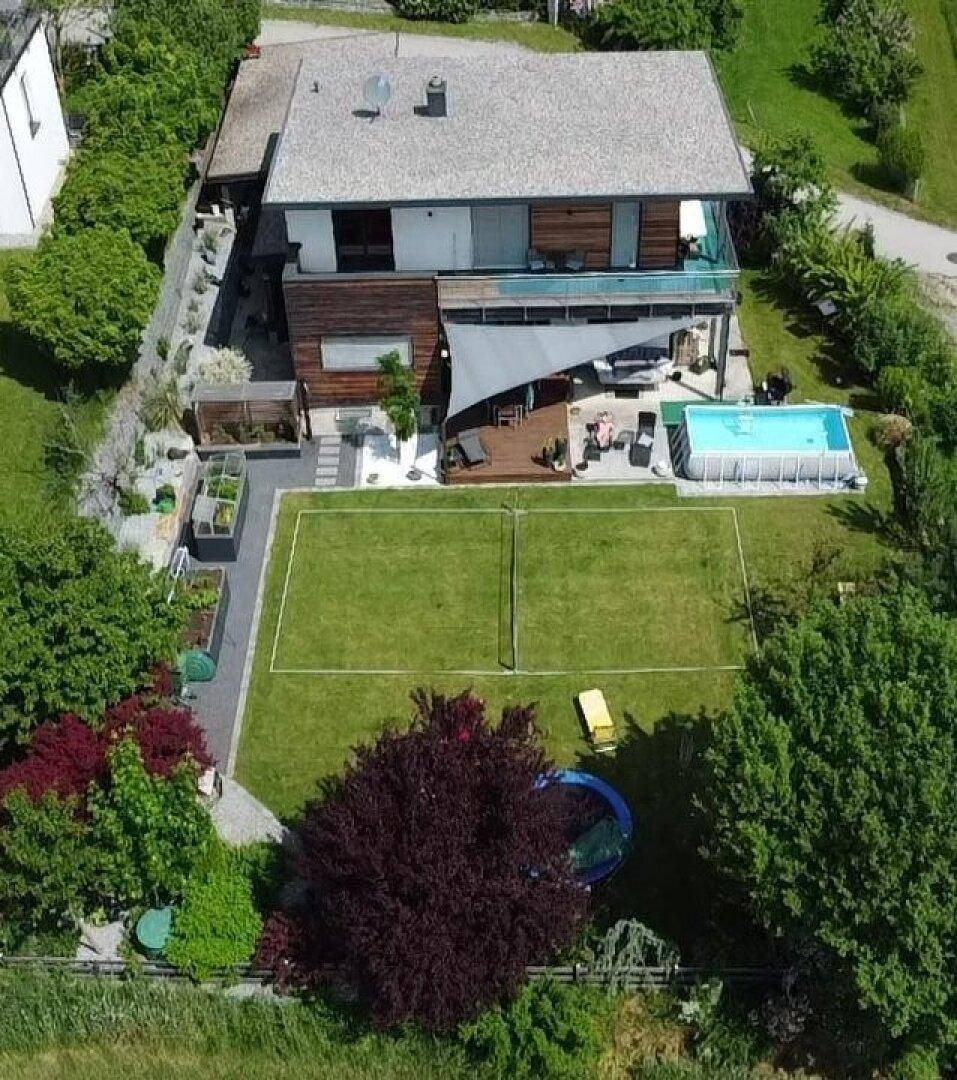 Vogelperspektive des Anwesens mit modernem Haus, Terrasse, Pool und einem Tennisplatz im Garten.