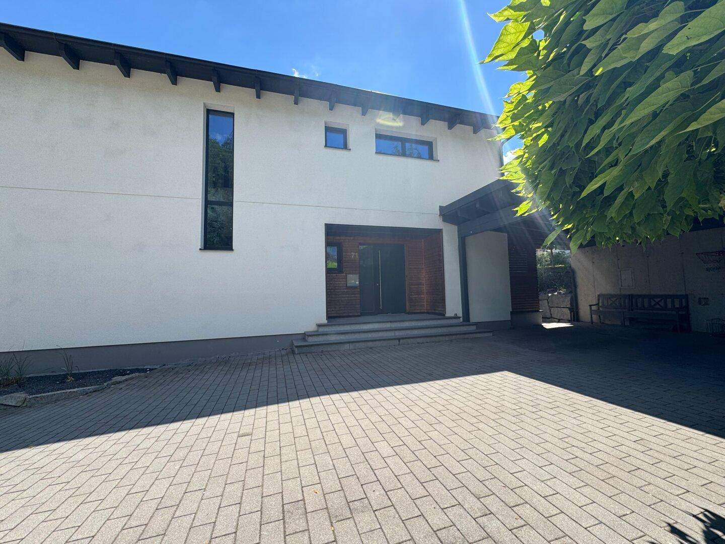 Moderne Hausfassade mit gepflastertem Eingangsbereich und großen, vertikalen Fenstern.