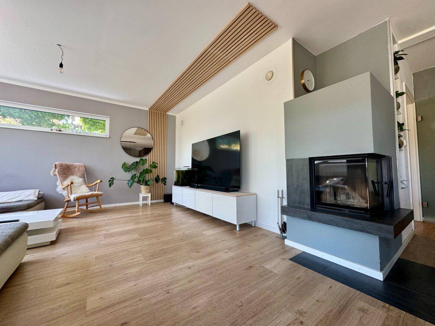 Helles Wohnzimmer mit modernem Kamin, Holzboden und stilvoller Einrichtung in Grau- und Weißtönen.
