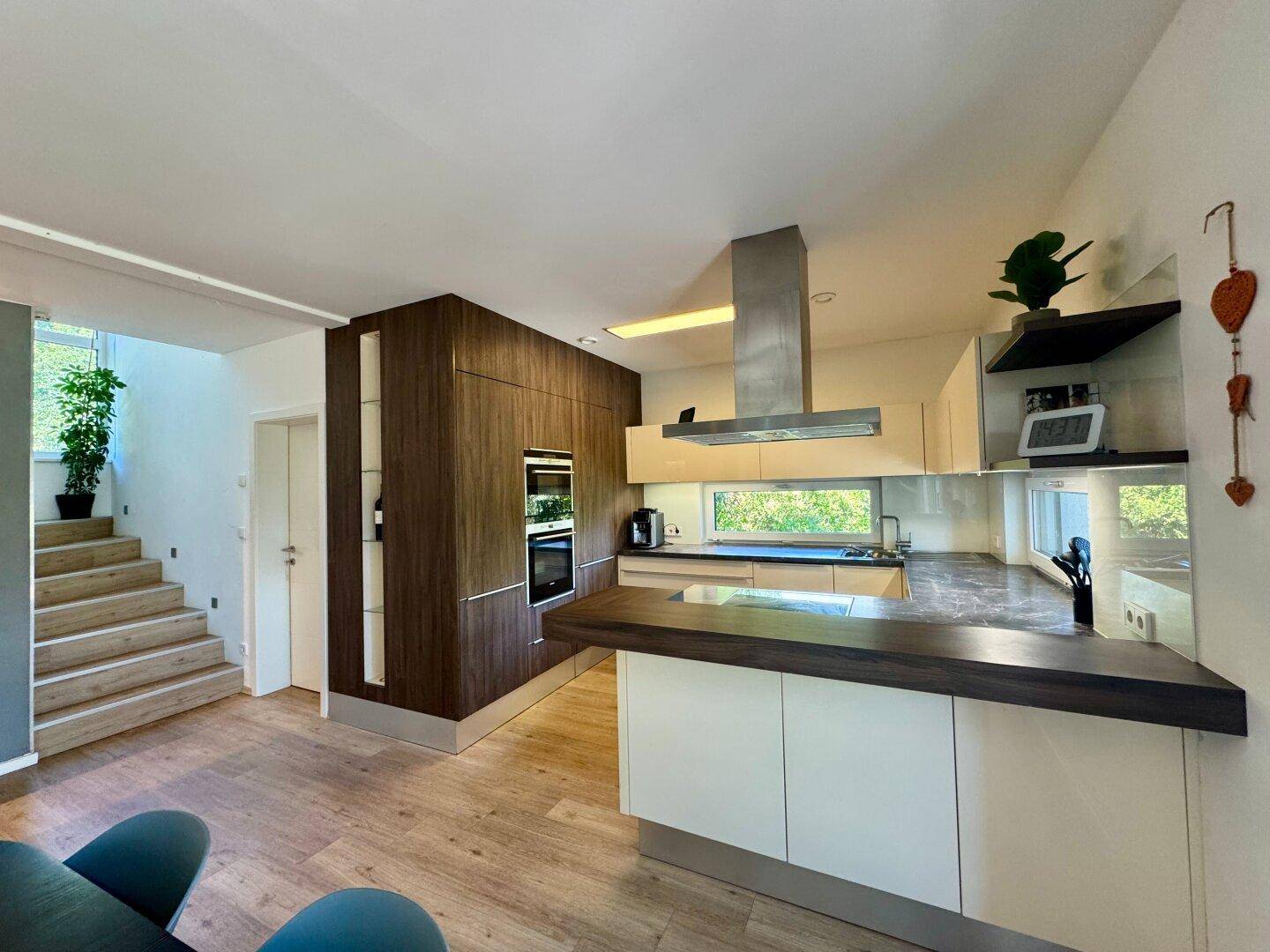 Moderne Einbauküche mit hellen und dunklen Holzfronten, integrierten Geräten und Kochinsel.