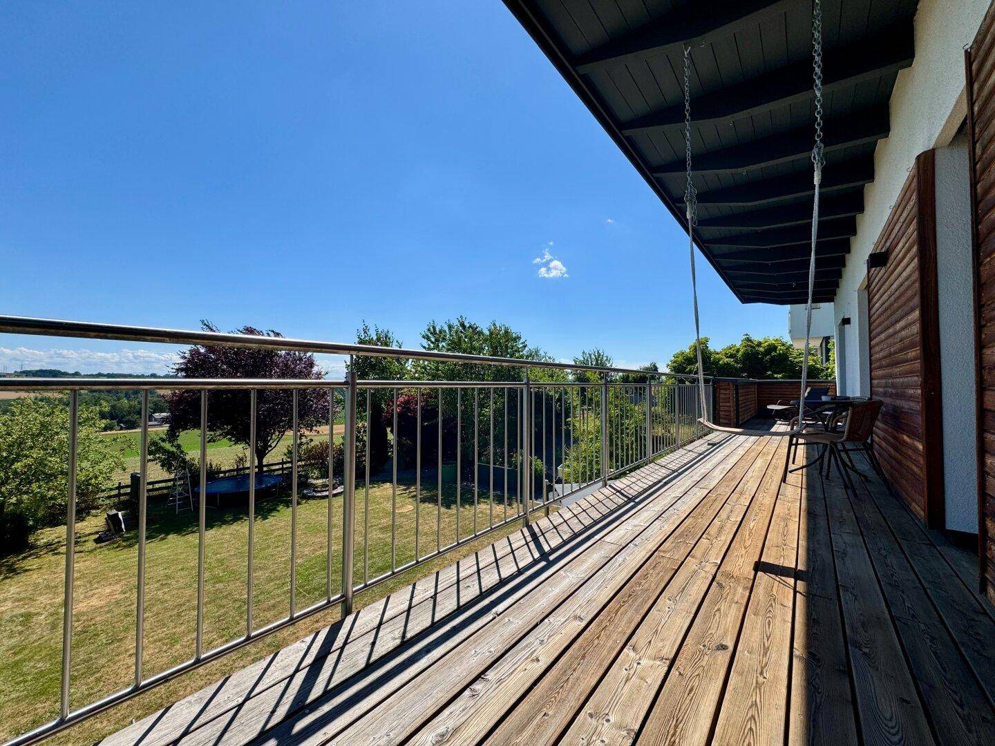 Geräumiger Balkon mit Holzboden und Metallgeländer bietet einen weiten Blick ins Grüne.