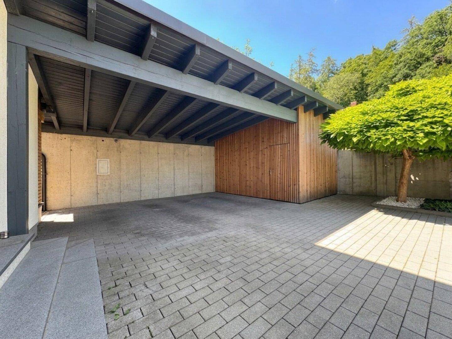 Überdachter Carport mit gepflastertem Boden und Holzkonstruktion für Fahrzeuge.