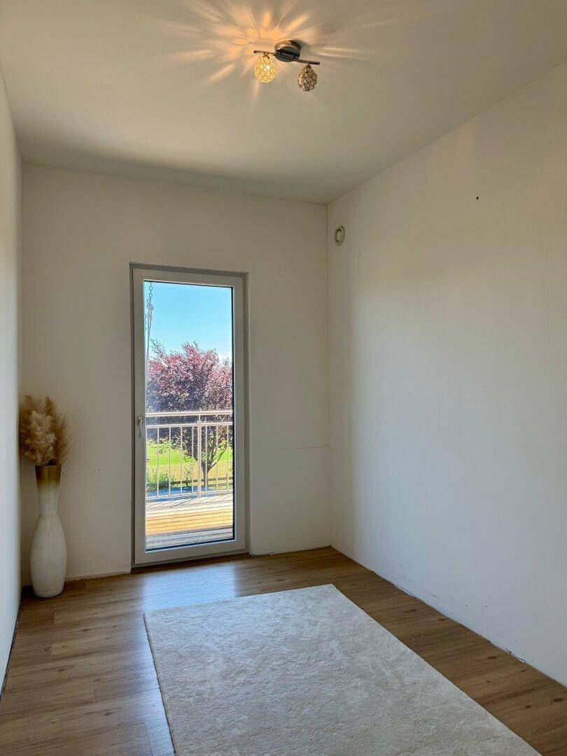 Helles Zimmer mit Holzboden, Teppich und Zugang zu einem französischen Balkon.