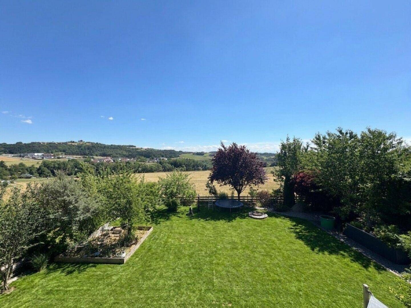 Weitläufiger Garten mit Trampolin und Blick über grüne Felder und sanfte Hügel in der Ferne.