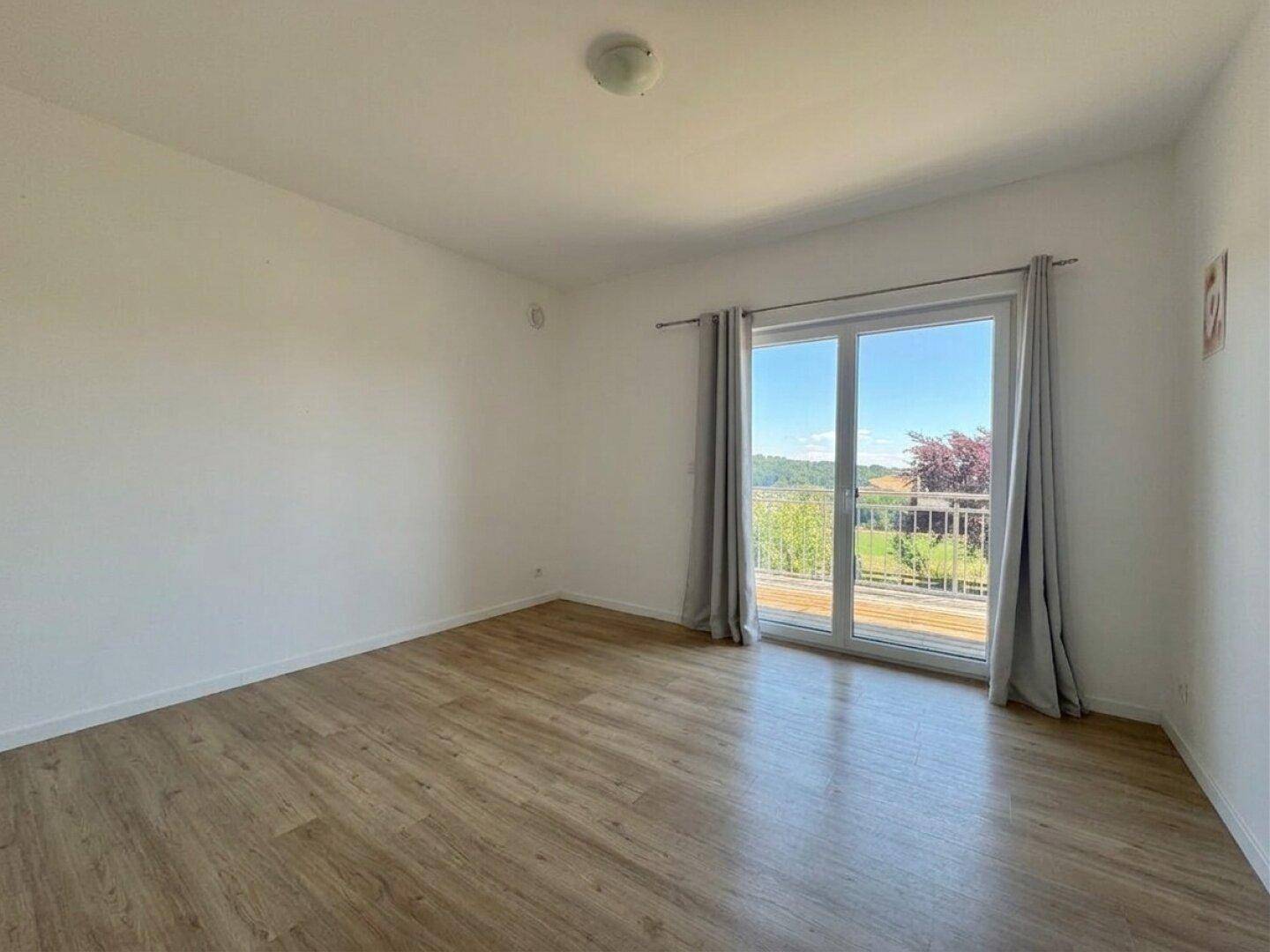 Helles Schlafzimmer mit Holzboden und großem Fenster mit Zugang zum Balkon.