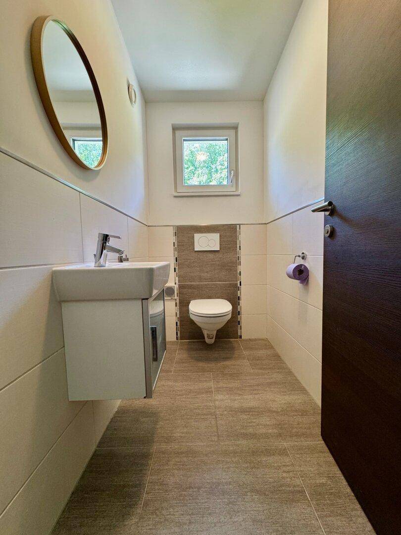 Kleines Gäste-WC mit modernem Waschbecken, Wand-WC und Fenster.