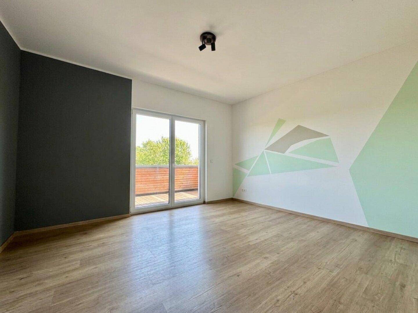 Helles Zimmer mit Holzboden und kreativer Wandgestaltung, mit Zugang zum Balkon.