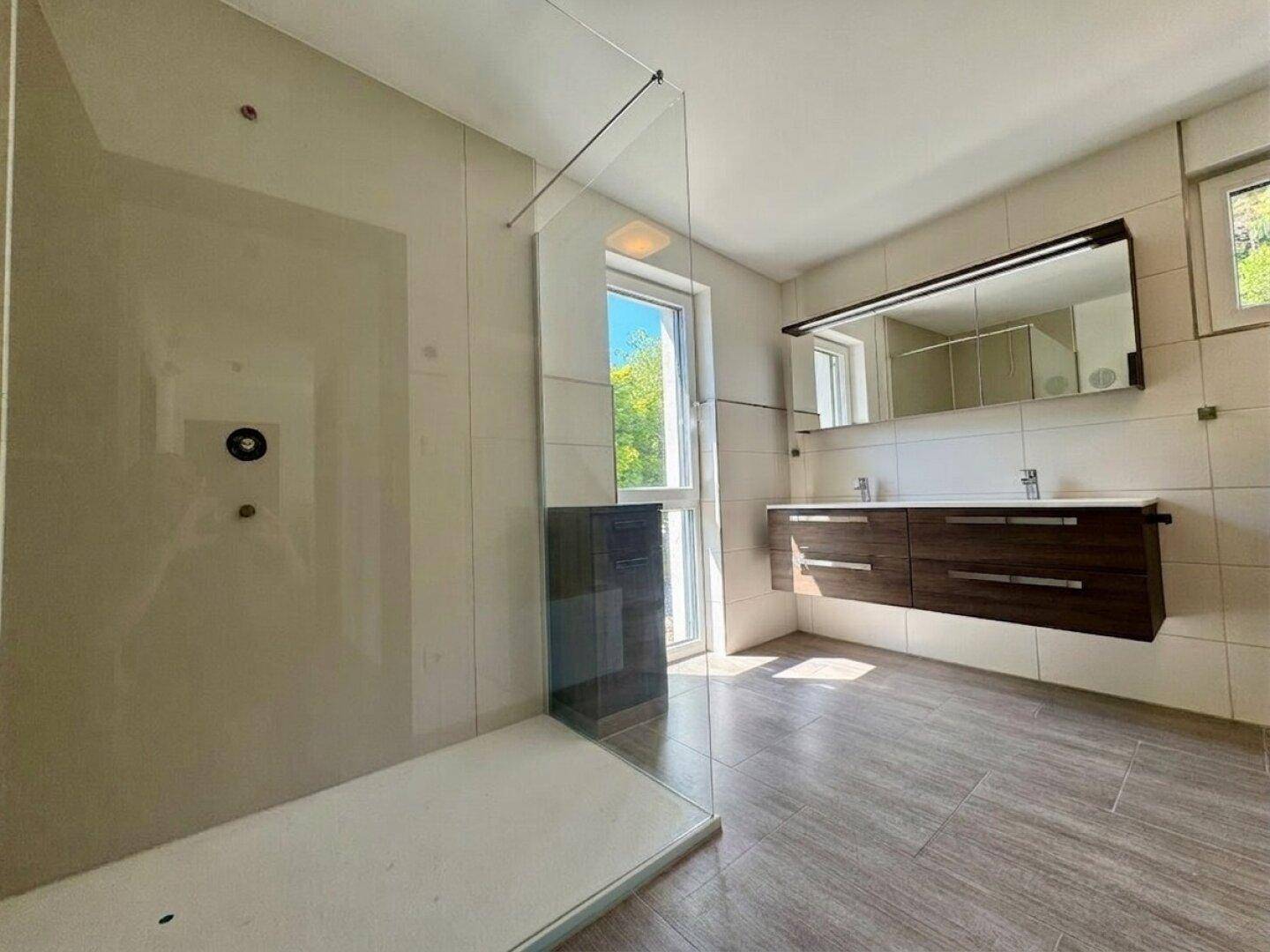 Modernes Badezimmer mit großer begehbarer Dusche, Doppelwaschbecken und Fenster.