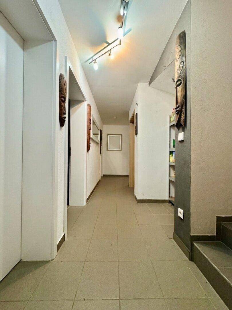 Langer Flur mit Fliesenboden und dekorativen Masken an den Wänden.