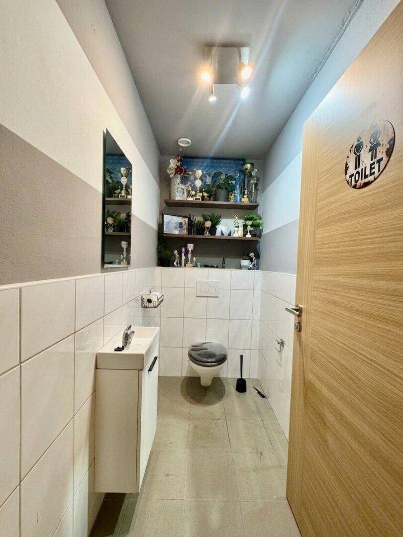Modernes Gäste-WC mit Waschbecken, Wand-WC und dekorativen Regalen.