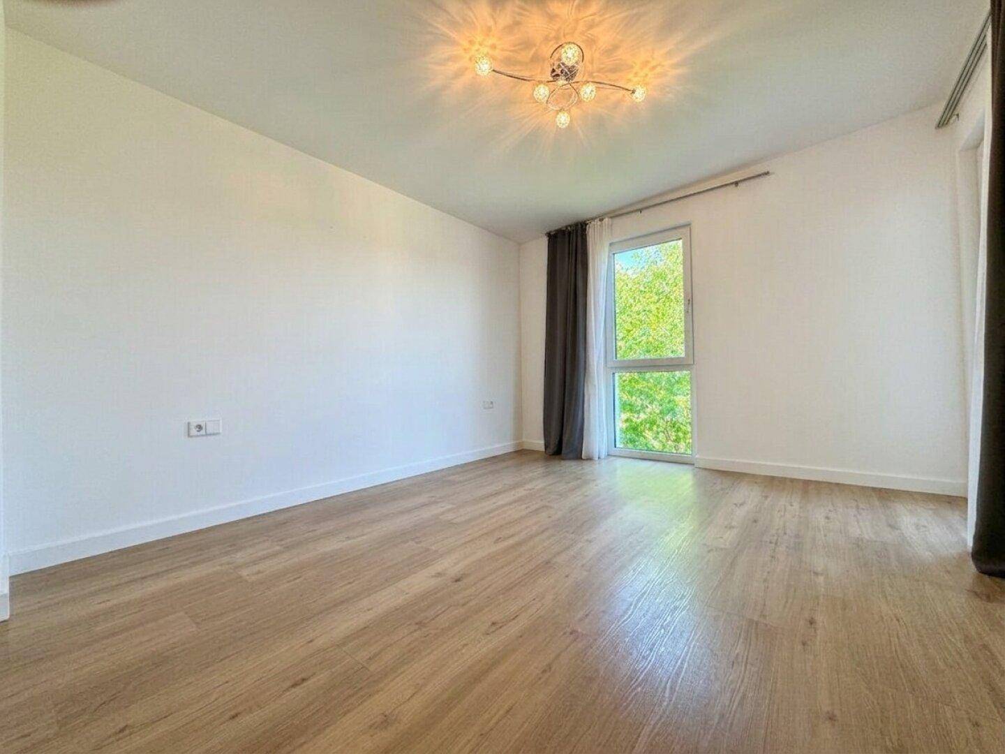 Geräumiges, helles Zimmer mit Holzfußboden und großem Fenster mit Blick ins Grüne.