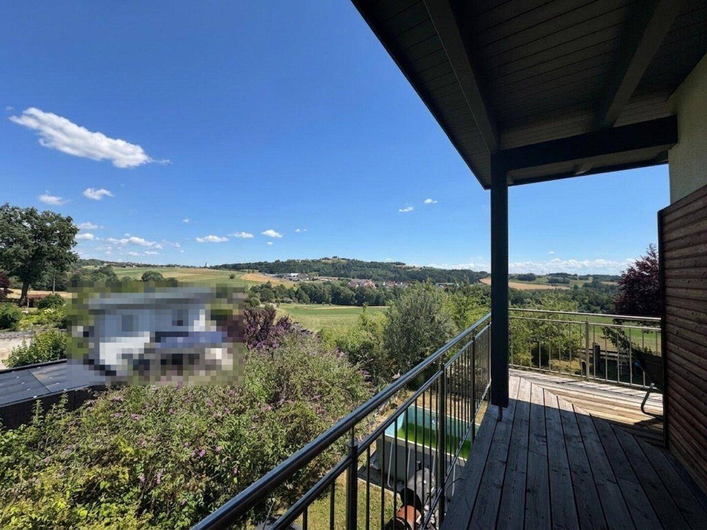 Sonniger Balkon mit Holzboden und weitem Blick über die ländliche Umgebung und grüne Hügel.