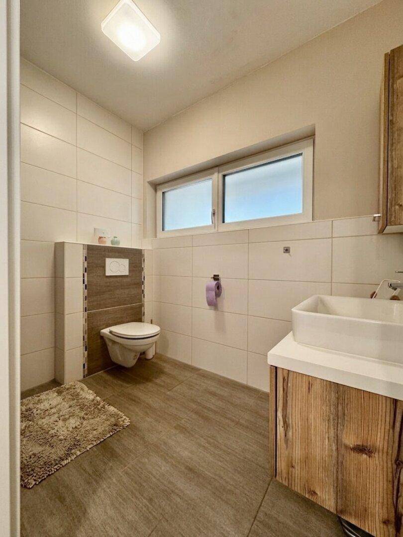 Modernes Gäste-WC mit Wand-WC, Waschbecken und Fenster für Tageslicht.