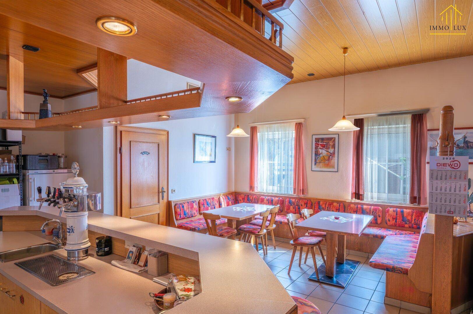Gemütlicher Restaurantbereich mit Holzbalkendecke, Theke und gepolsterten Sitzbänken.