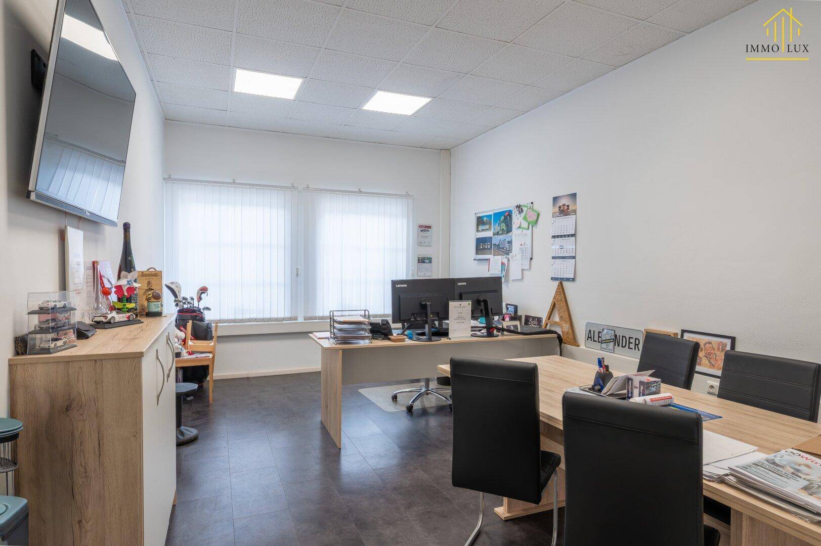 Funktionales Büro mit Schreibtischen, Bürostühlen und einem großen Fenster für Tageslicht.