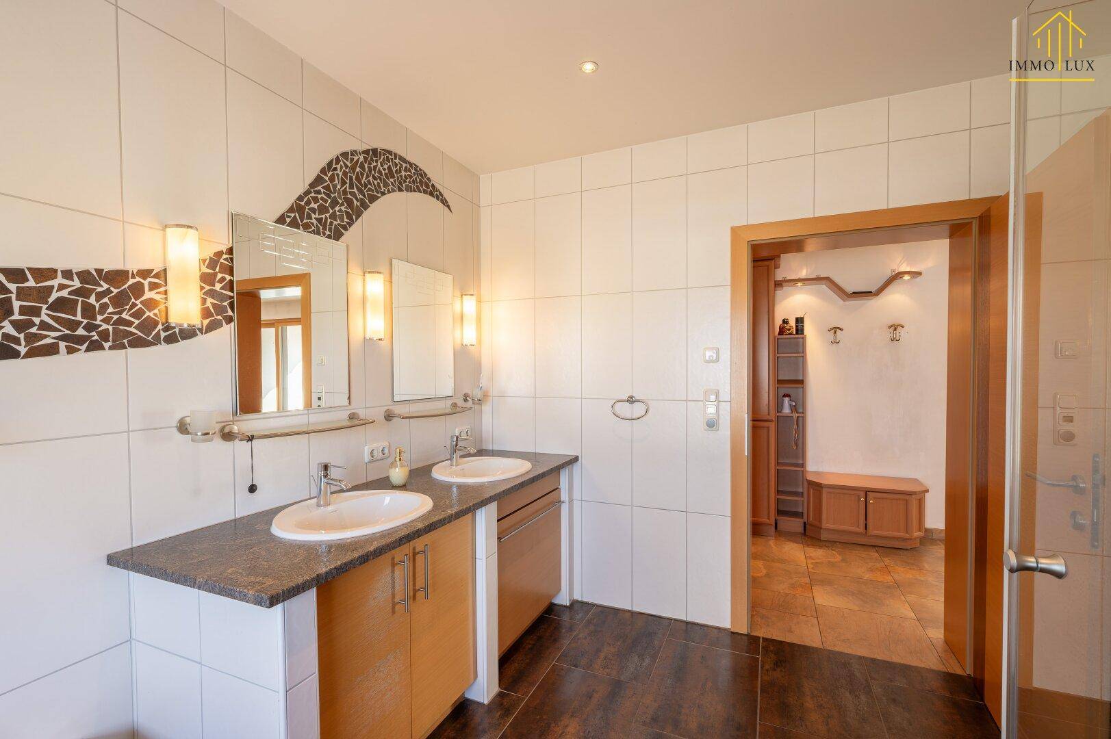 Badezimmer mit Doppelwaschtisch, Fliesen an Wänden und Boden sowie dekorativen Spiegelleuchten.