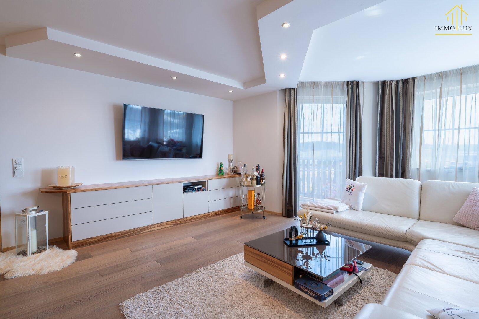 Geräumiges Wohnzimmer mit bequemer Couch, Holzboden und Blick ins Grüne.