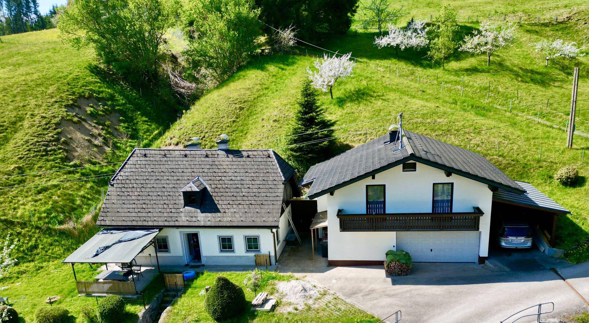 Luftaufnahme von zwei Häusern auf einem grünen Hügel mit umliegender Naturlandschaft.