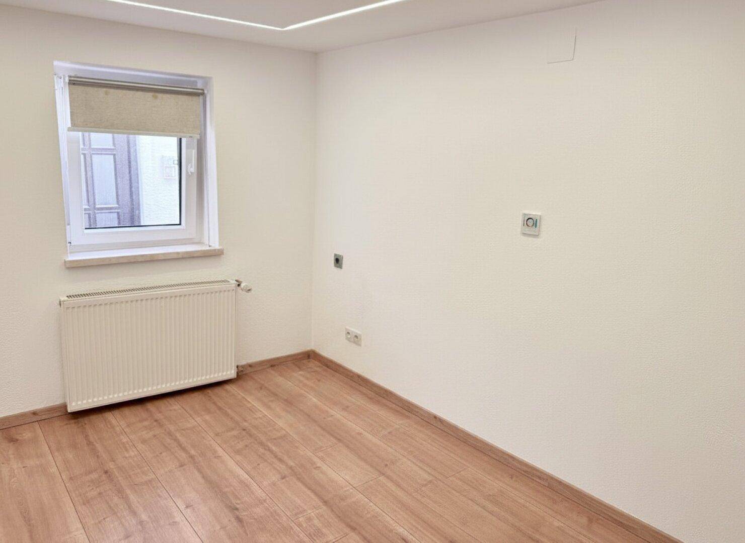 Helles Zimmer mit Laminatboden, weißen Wänden und einem Fenster, ideal als Schlaf- oder Arbeitszimmer.