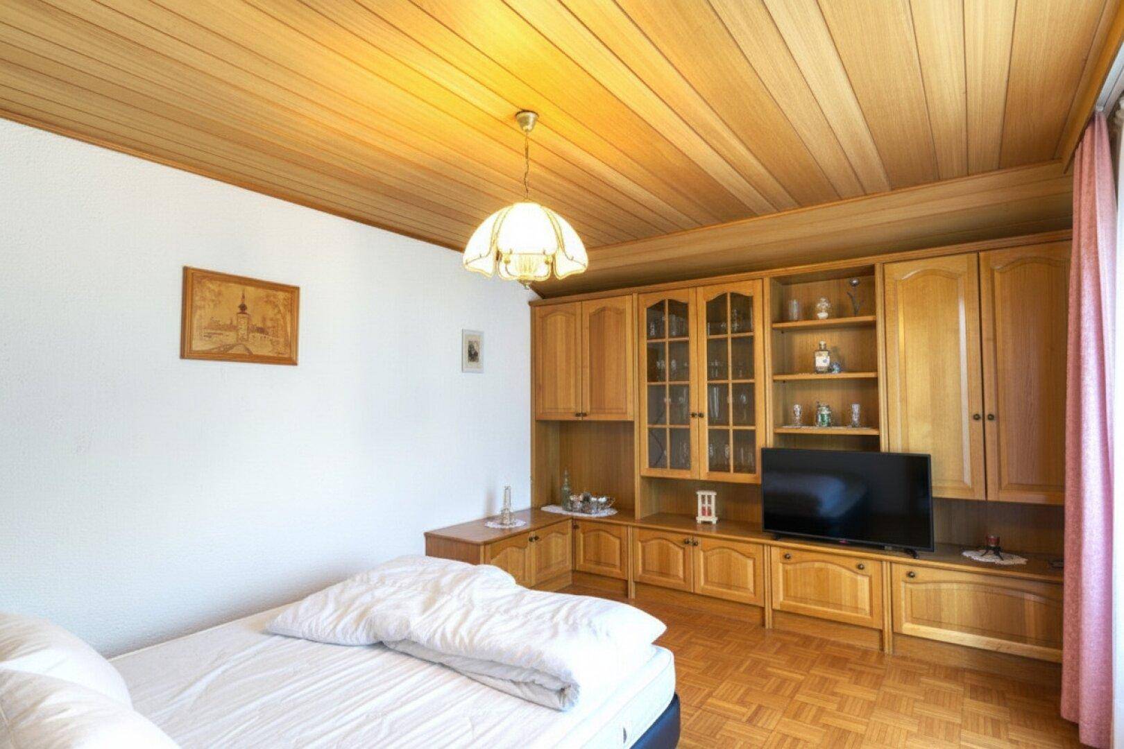 Gemütliches Schlafzimmer mit Holzdecke, Parkettboden und einer großen Schrankwand mit TV-Bereich.