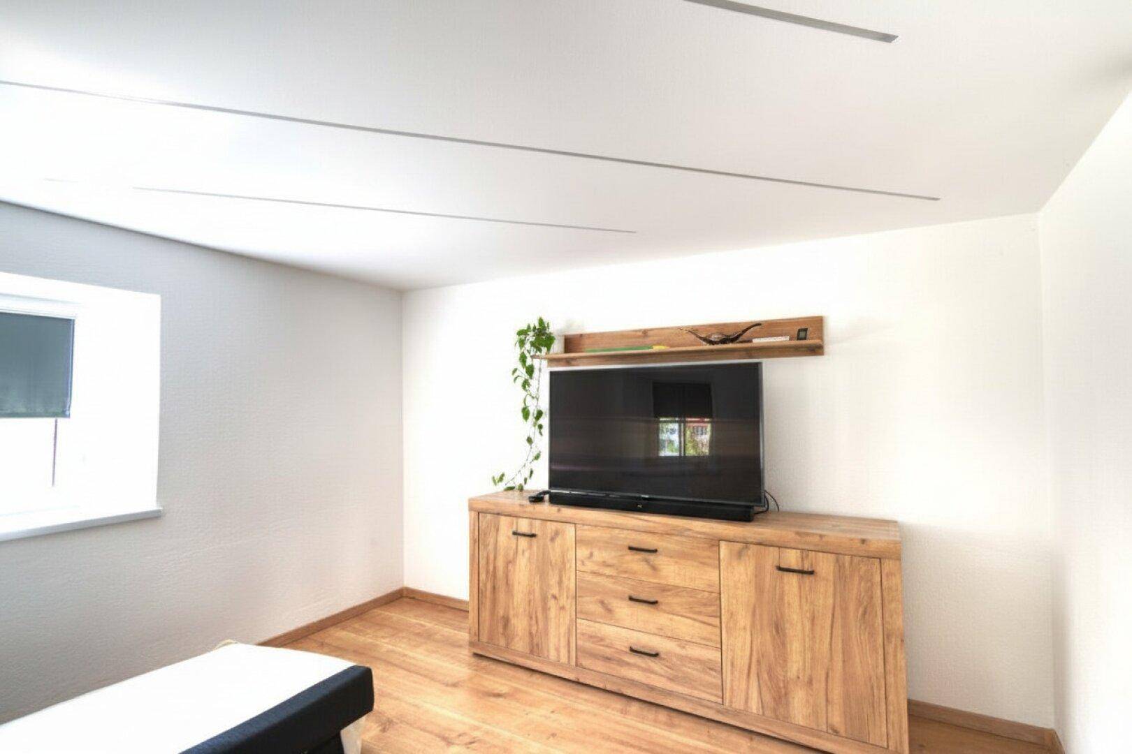 Heller Wohnbereich mit modernem Holz-Sideboard, großem Fernseher und Laminatboden.