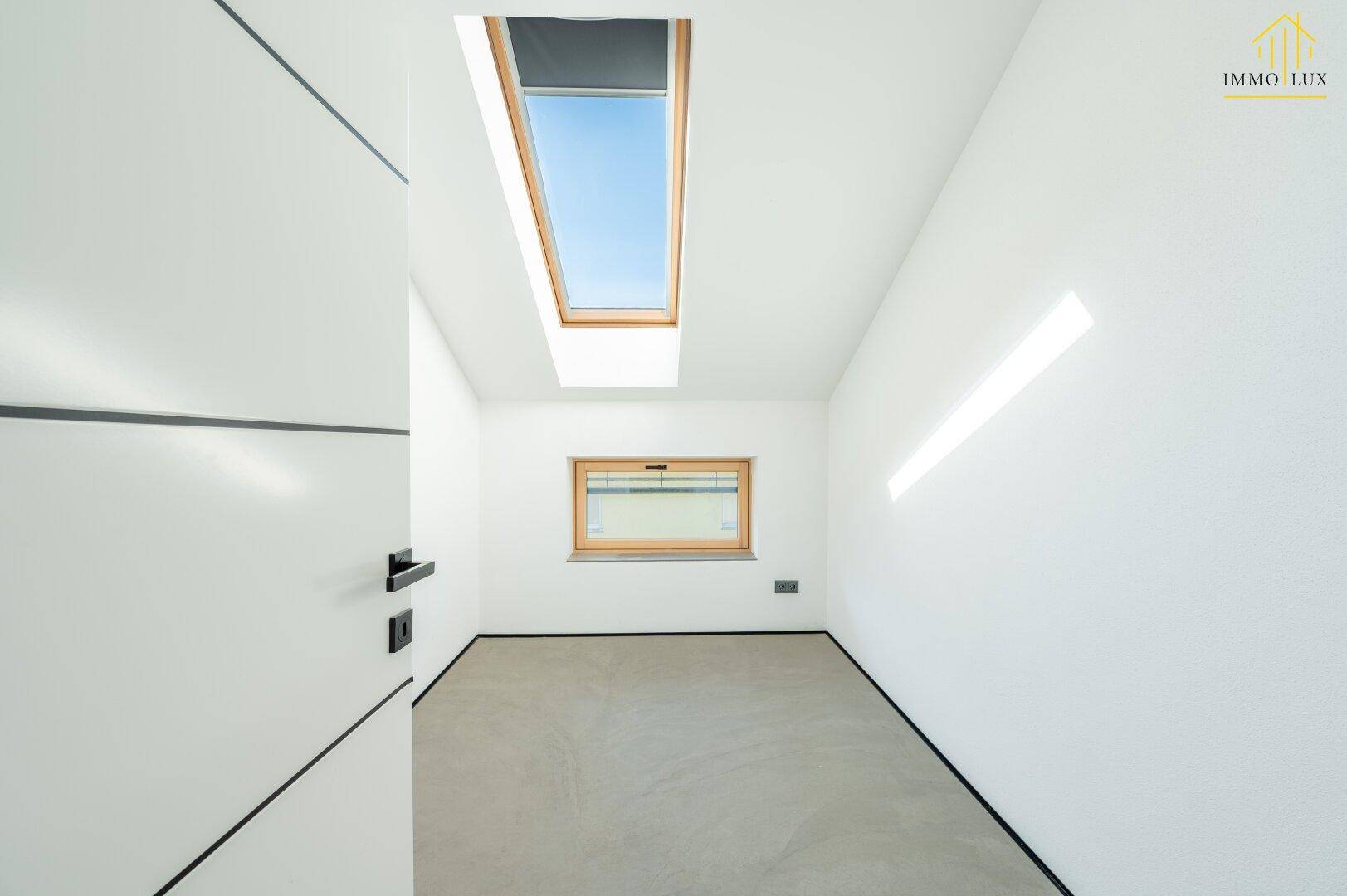 Helles Zimmer mit Dachfenster, kleinem Fenster und weiß gestrichenen Wänden.