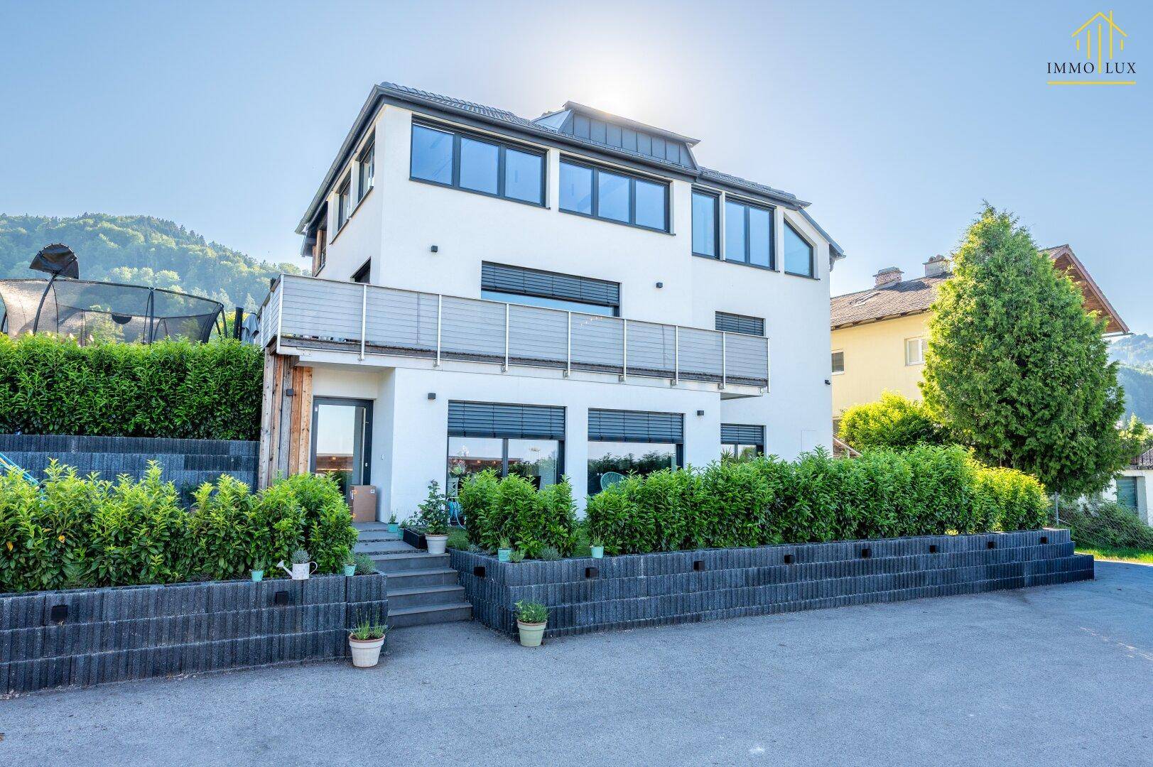 Modernes Wohnhaus mit Balkon, gepflegter Hecke und Bergblick.