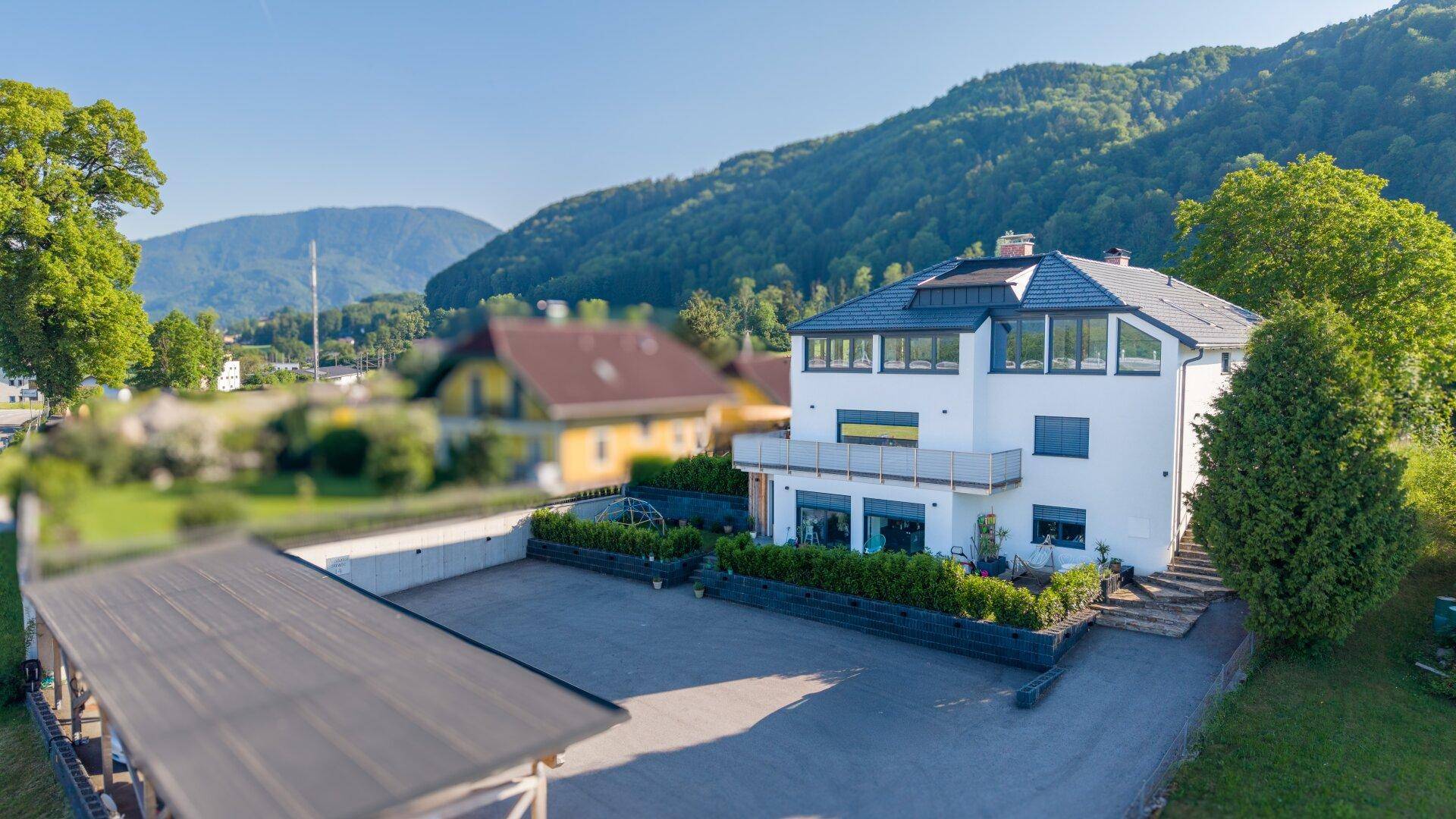 Luftaufnahme eines modernen Wohnhauses mit großem Parkplatz und Bergblick.