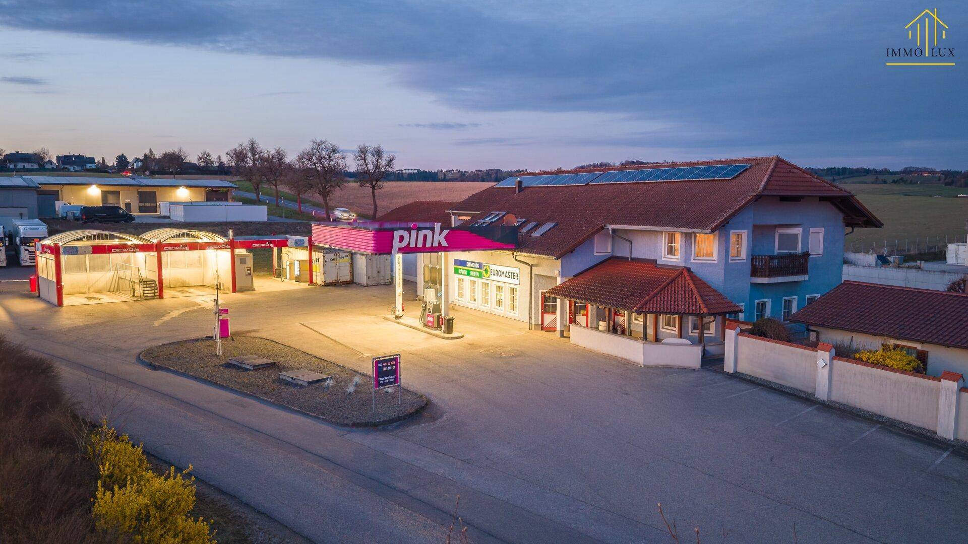 Luftaufnahme der Tankstelle und des Gebäudes mit Solaranlage auf dem Dach bei Dämmerung.