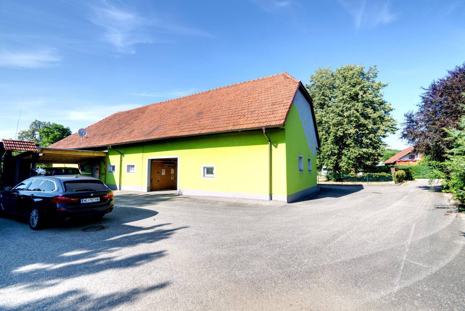 Ansicht des Gebäudes mit leuchtend grüner Fassade, rotem Ziegeldach und großem Vorplatz mit Parkmöglichkeiten.