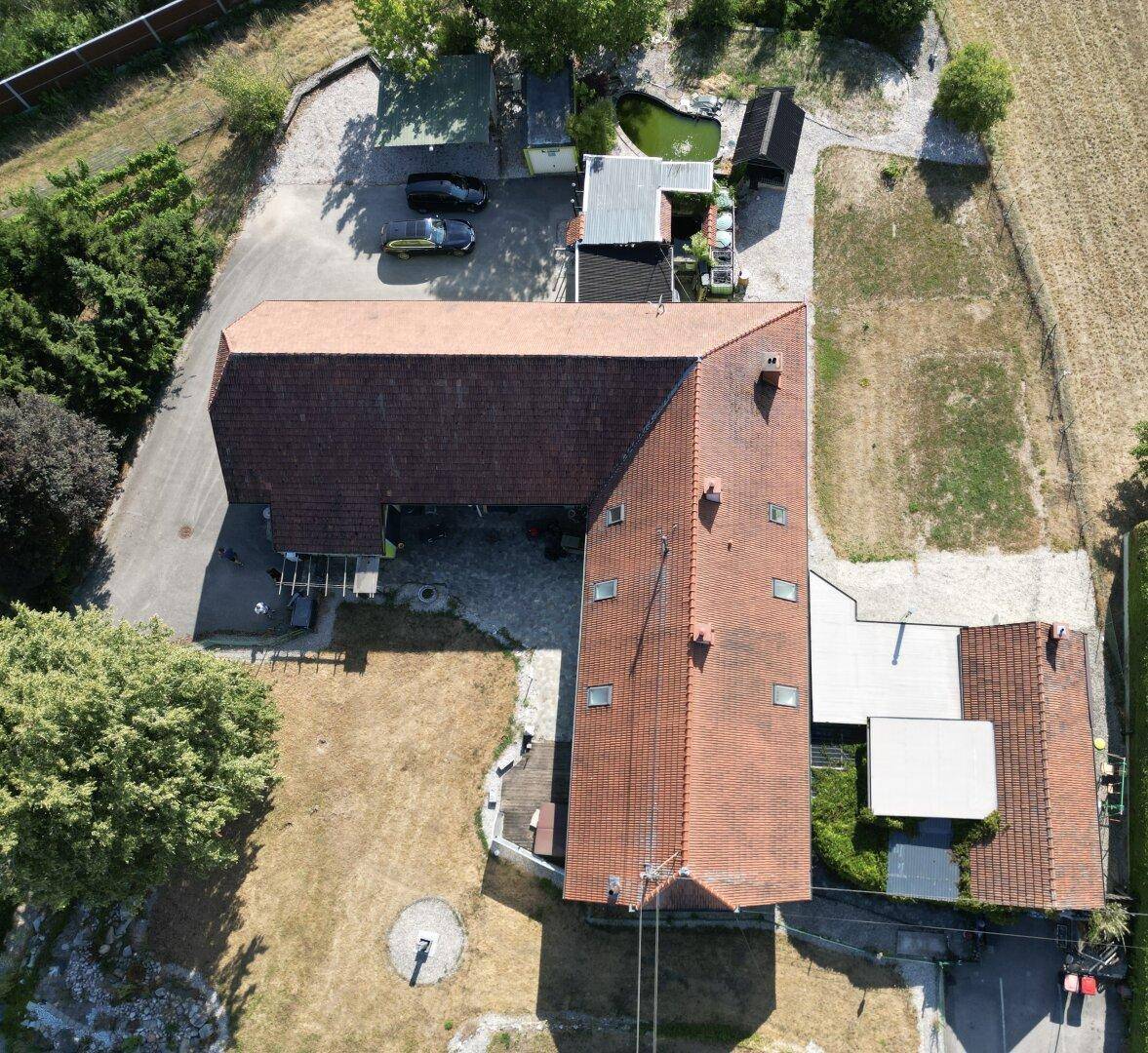 Draufsicht des L-förmigen Gebäudes mit rotem Ziegeldach und angrenzenden Freiflächen.
