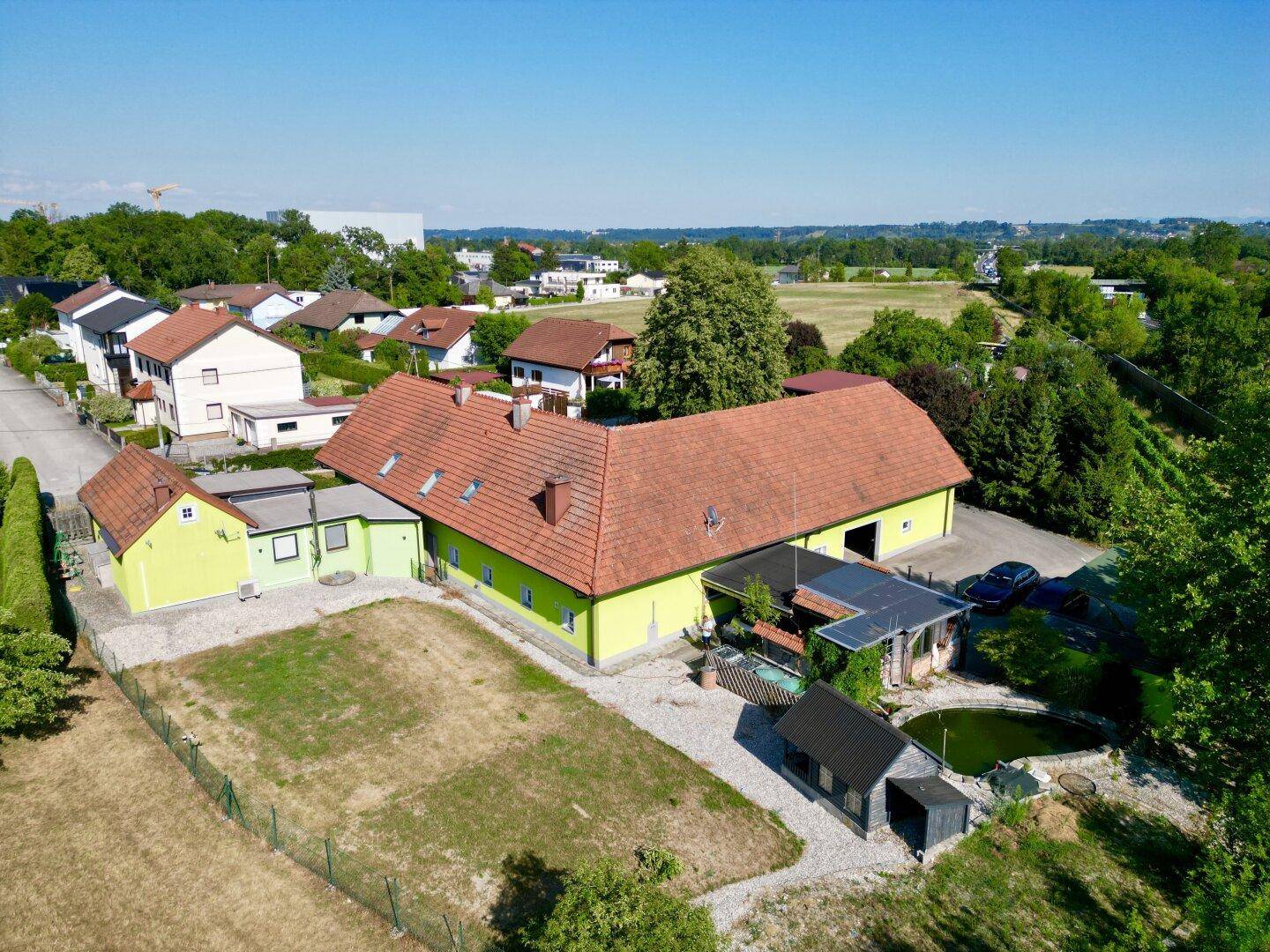 Luftaufnahme des Anwesens mit Teich, Hauptgebäude und umliegender Wohnbebauung sowie Feldern.