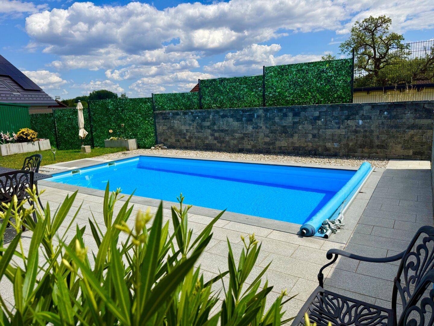 Großer, rechteckiger Swimmingpool im Gartenbereich mit gepflasterter Umrandung und grüner Hecke im Hintergrund.