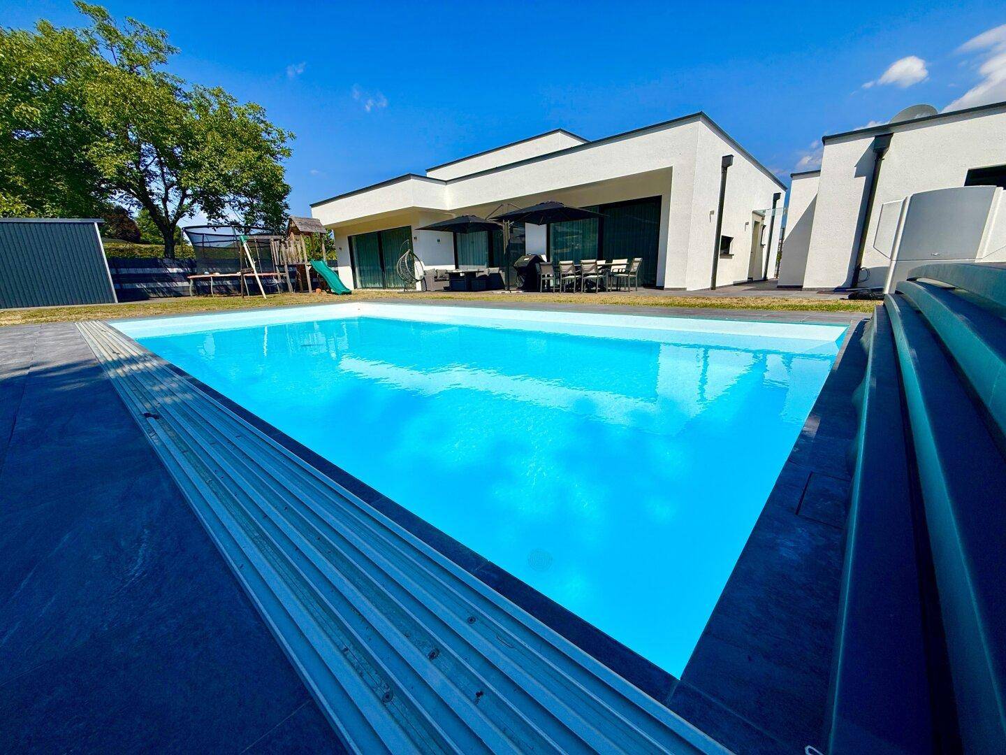 Außenansicht des modernen Hauses mit großem Swimmingpool und klarem blauen Wasser an einem sonnigen Tag.