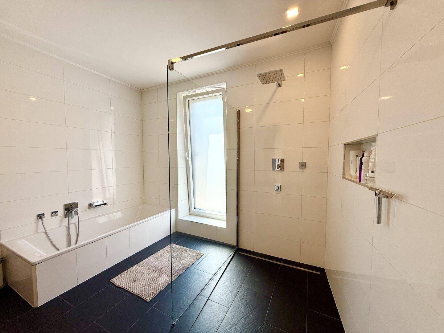 Helles Badezimmer mit Badewanne, geräumiger begehbarer Dusche und Regendusche für entspannende Momente.
