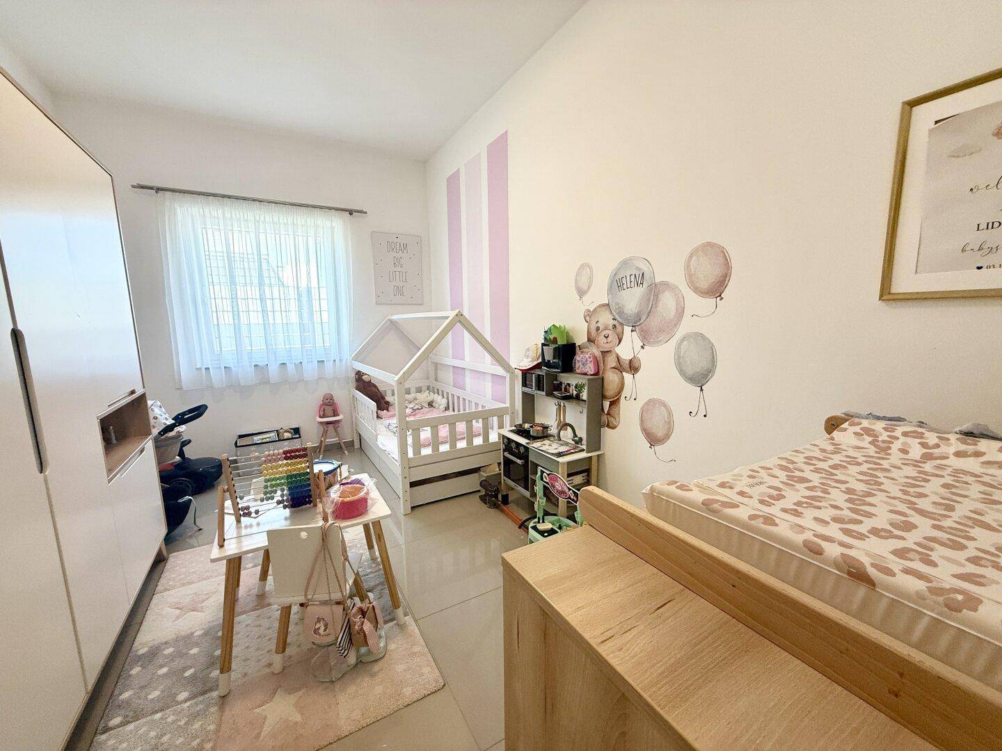 Freundliches Kinderzimmer mit Babybett, Spielbereich und farbenfrohen Wanddekorationen für kleine Bewohner.