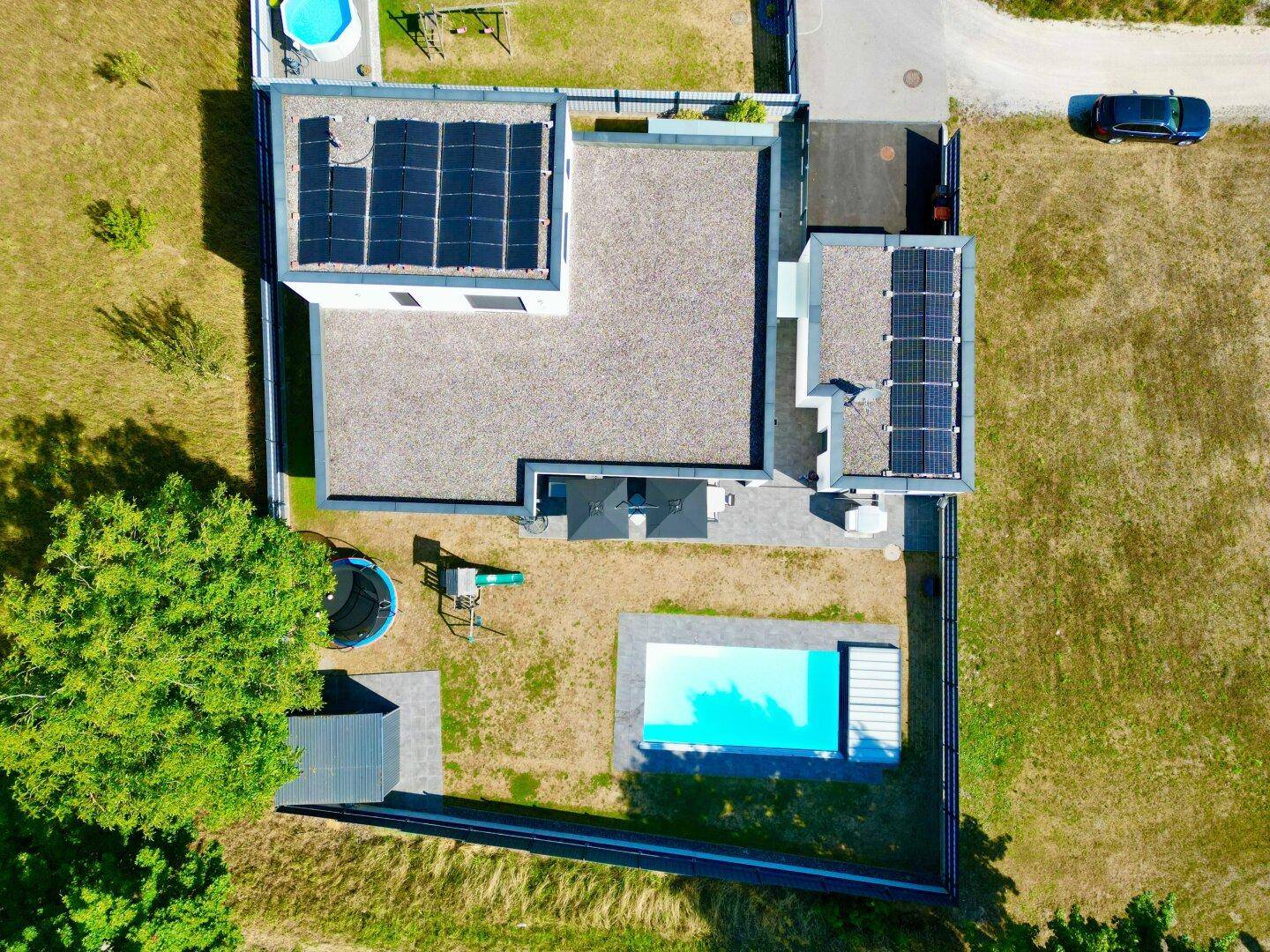 Vogelperspektive des Anwesens mit modernem Haus, Pool, Garten und Photovoltaikanlage auf dem Dach.