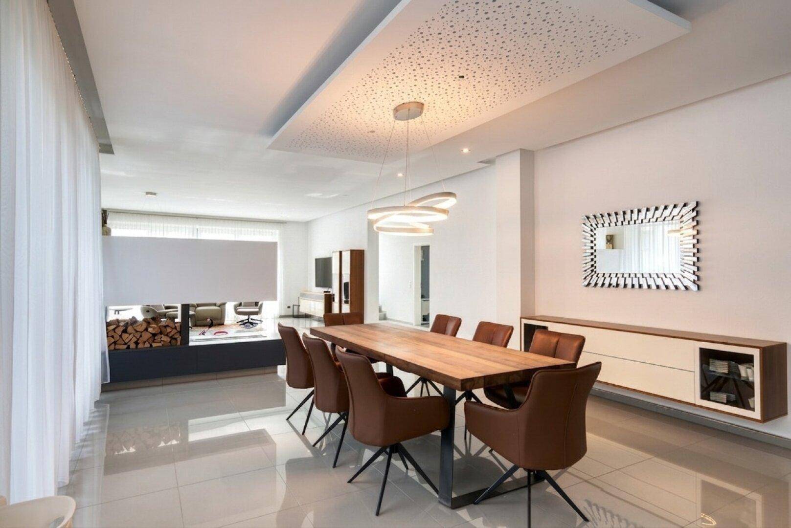 Eleganter Essbereich mit großem Holztisch, modernen Stühlen und dekorativer Deckenbeleuchtung.