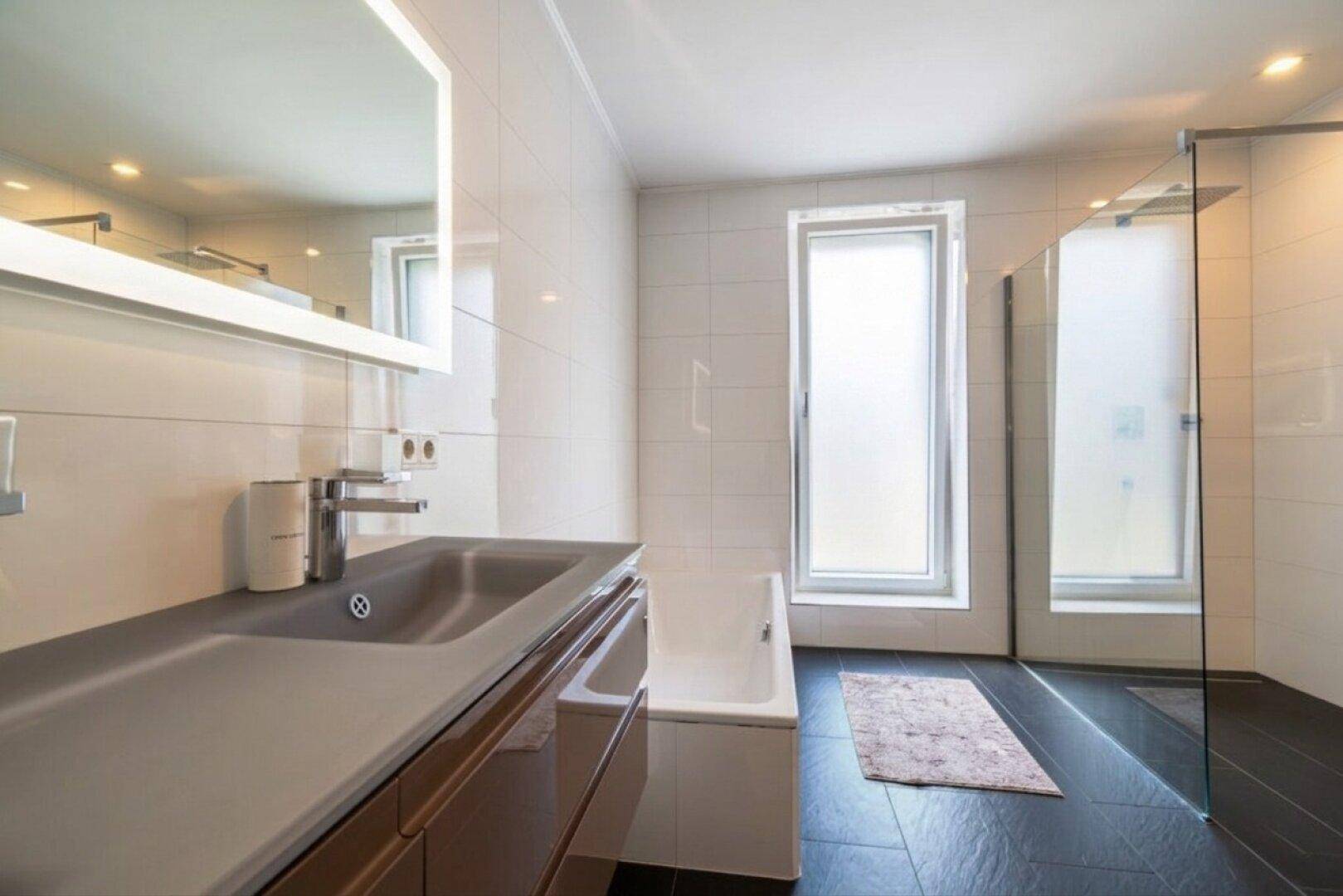 Modernes Badezimmer mit Waschtisch, Badewanne, Dusche und einem hohen Fenster für natürliche Belüftung.