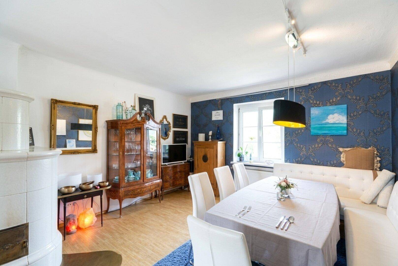 Gemütlicher Essbereich mit großem Tisch, Kachelofen und dekorativer blauer Tapete.