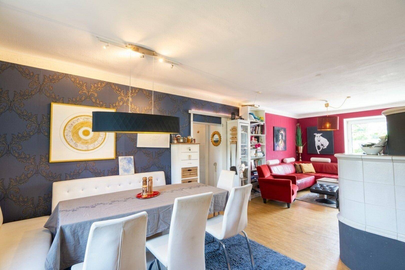 Offener Wohn- und Essbereich mit Kachelofen, rotem Sofa und farbenfroher Wandgestaltung.