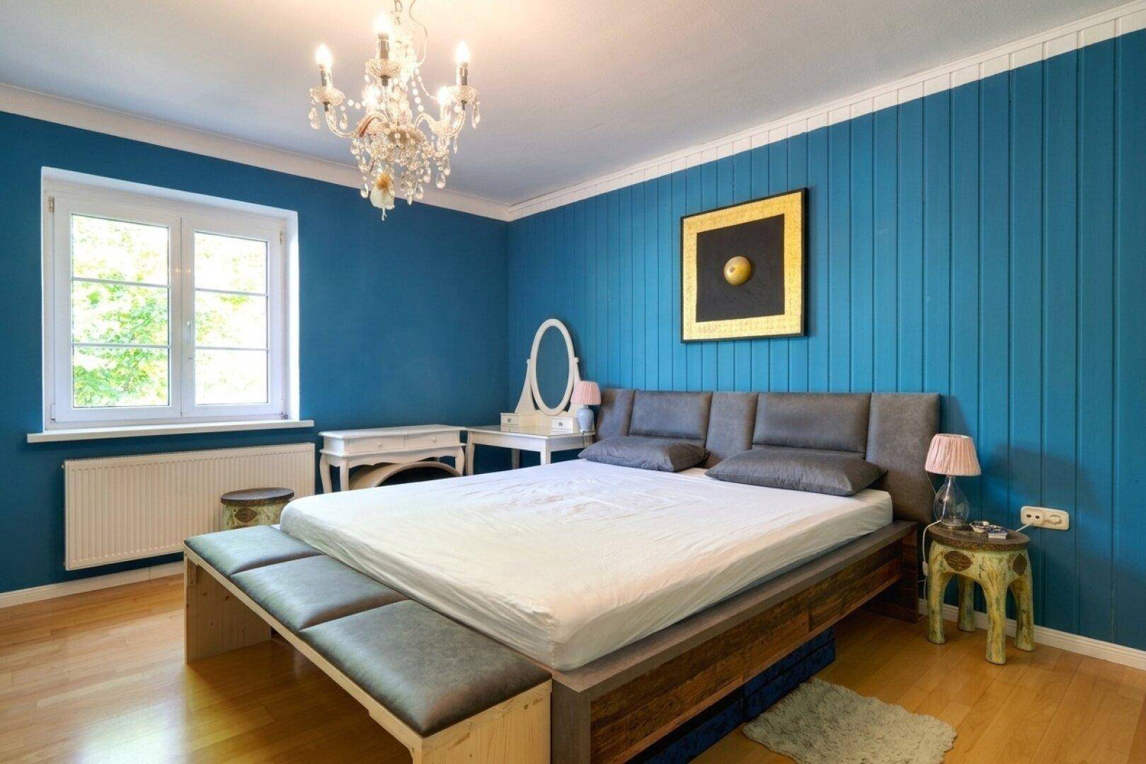 Schlafzimmer mit blauen Holzpaneelen, Doppelbett und einem Kronleuchter für eine elegante Atmosphäre.
