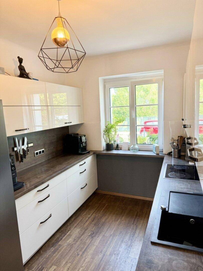 Moderne Küche mit weißen Hochglanzschränken, dunkler Arbeitsplatte und Fenster für Tageslicht.