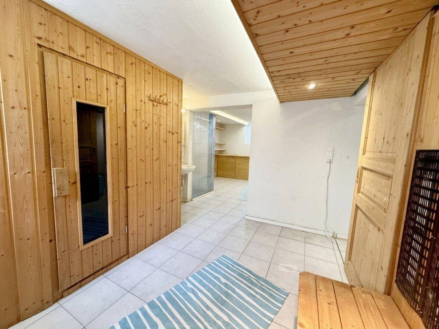 Wellnessbereich im Untergeschoss mit Sauna, gefliestem Boden und Holzverkleidung.