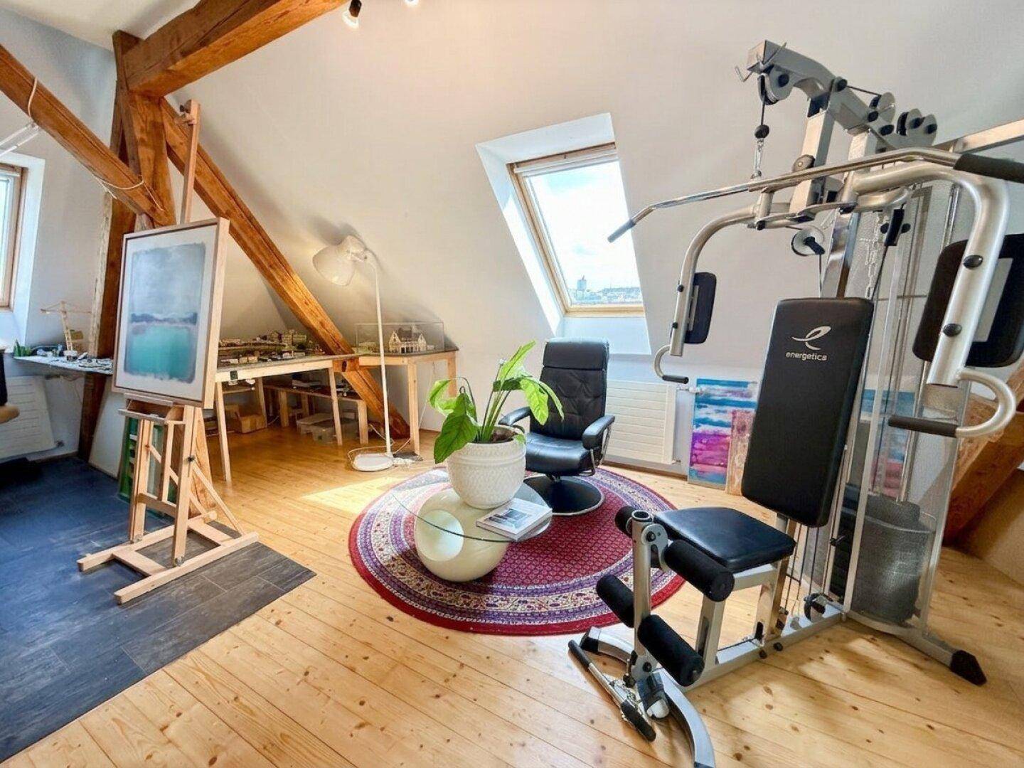 Helles Dachgeschosszimmer mit Holzbalken, Dachfenster und Fitnessgeräten, vielseitig nutzbar.