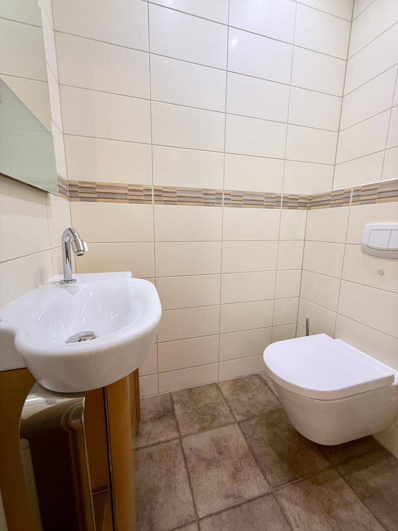 Kleines Gäste-WC mit Wand-WC, Waschbecken und hellen Fliesen.